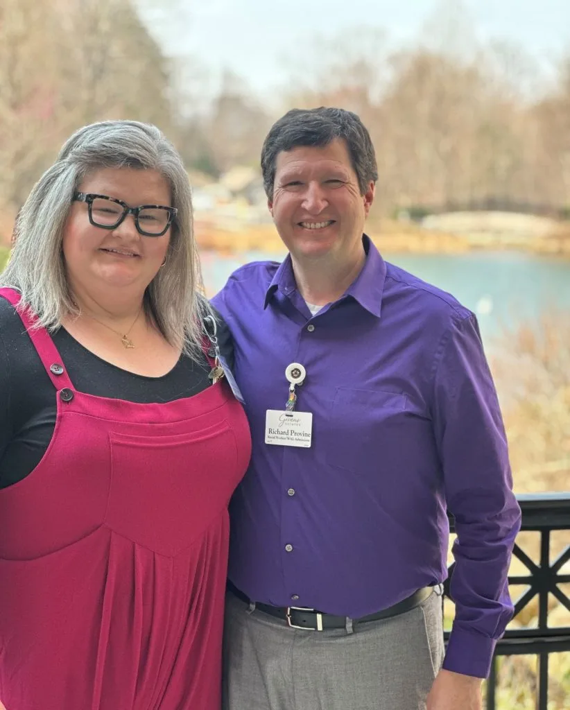Two people smiling outdoors near a lake