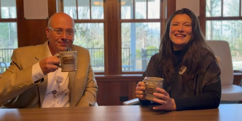 Two people smiling and holding coffee mugs indoors
